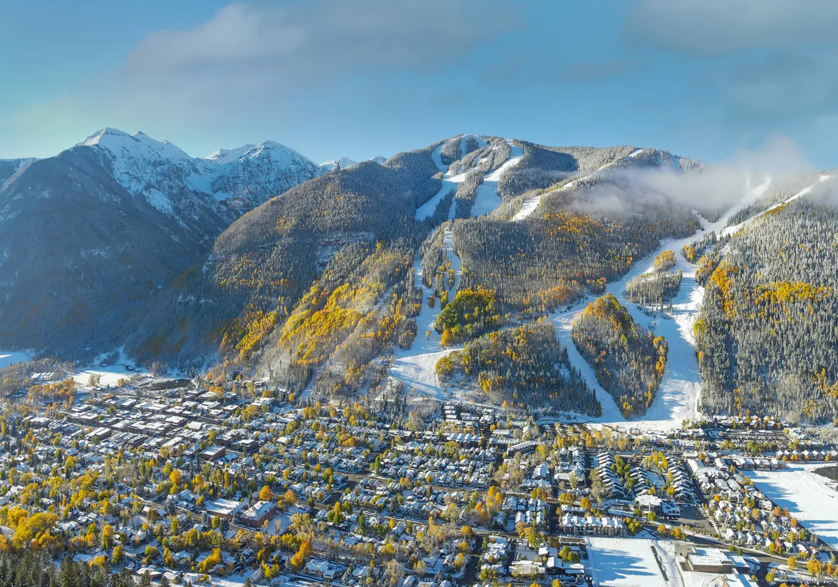 A panoramic view of Telluride featuring majestic mountains, ski slopes, the town nestled below, and autumn foliage. The image showcases the natural beauty and recreational opportunities, inviting families to venture outdoors and experience the scenic surroundings together.