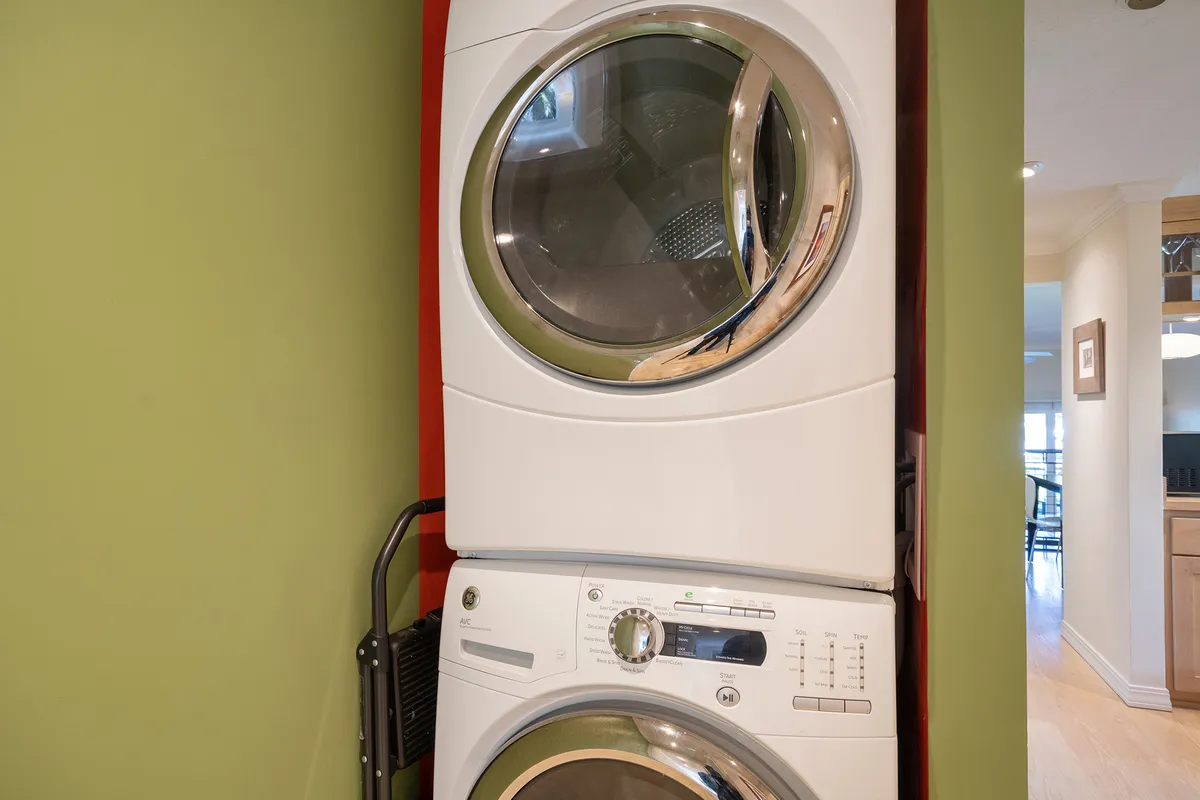 A compact laundry nook with stacked washer and dryer units against a green wall accented by chrome fixtures. The space feels tidy and efficient, highlighting practical amenities for extended stays or family visits.