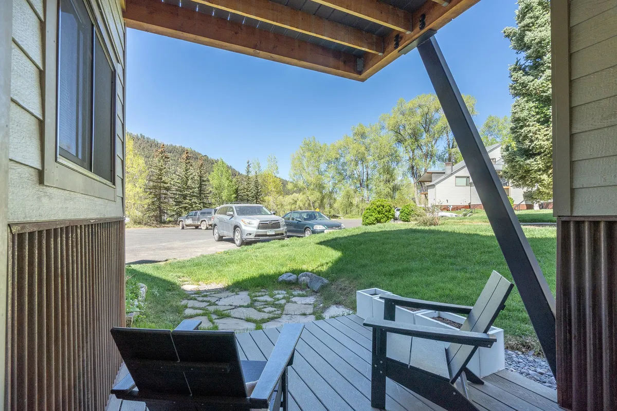 A view of outdoor deck chairs positioned on a stone pathway amidst surrounding greenery, with vehicles visible in the driveway. The scene suggests ease of access and ample parking, as well as opportunities for outdoor relaxation and social gatherings in a natural setting.