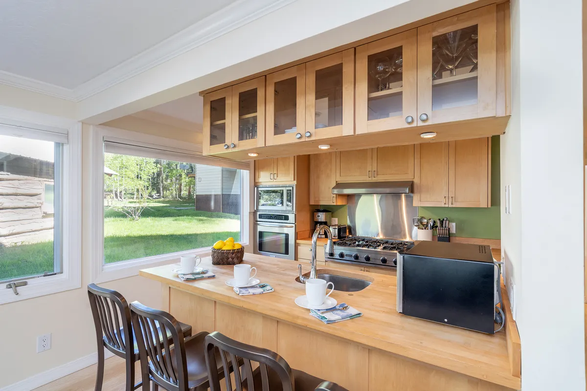 A warmly lit kitchen featuring a spacious island with seating, a sink, stove, and large windows that fill the space with natural light. The open layout allows for easy movement and conversation, ideal for cooking, entertaining, and family gatherings. There are hints of people preparing food and interacting in the space, emphasizing togetherness and comfort.