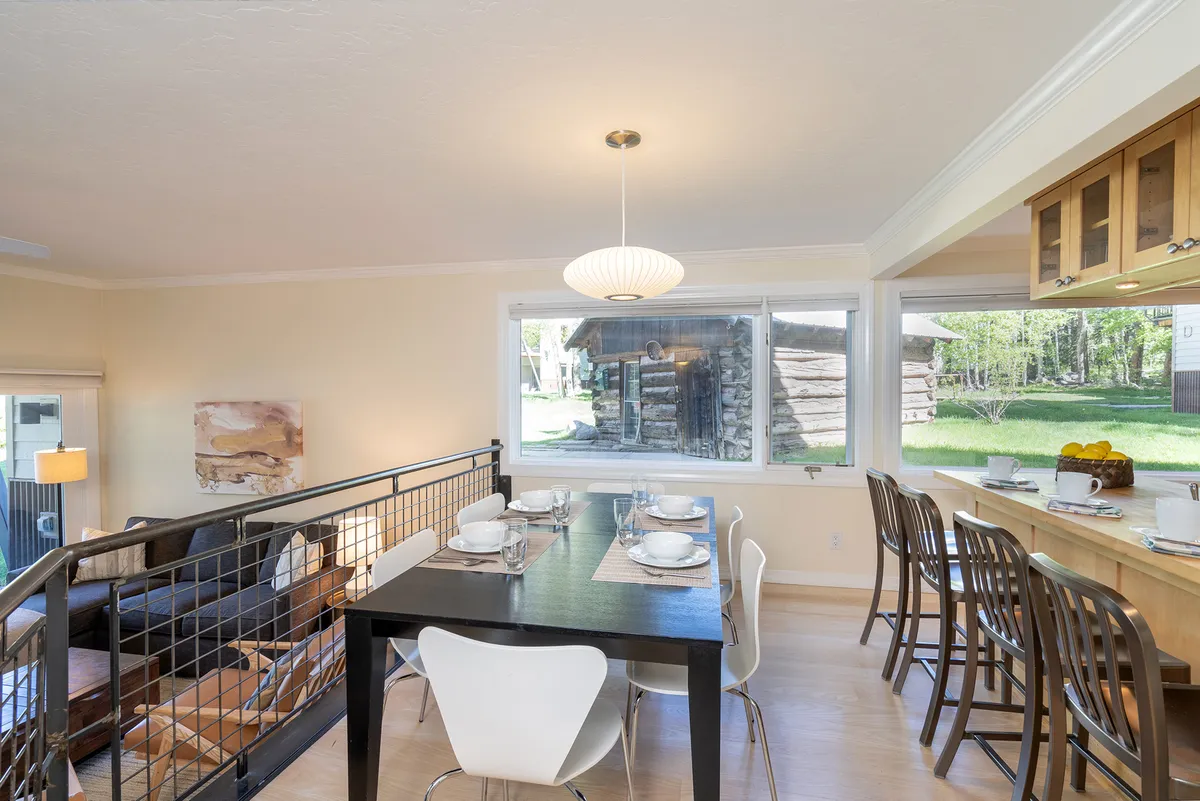 A cozy dining table set near a large window, adjacent to the kitchen counter. The scene is set for a family meal, with ample space for guests to gather, enjoy food, and take in views of the outdoors. Natural light pours in, making the space inviting for social gatherings, family meals, and intimate dining experiences.